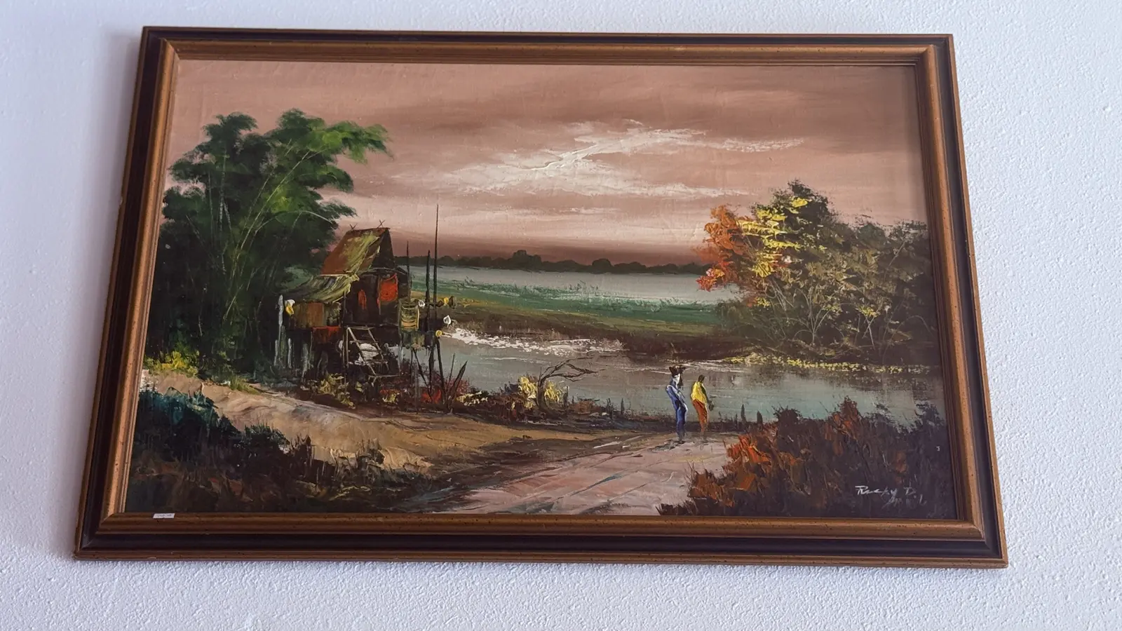 Framed landscape painting of a riverside cabin at dusk.