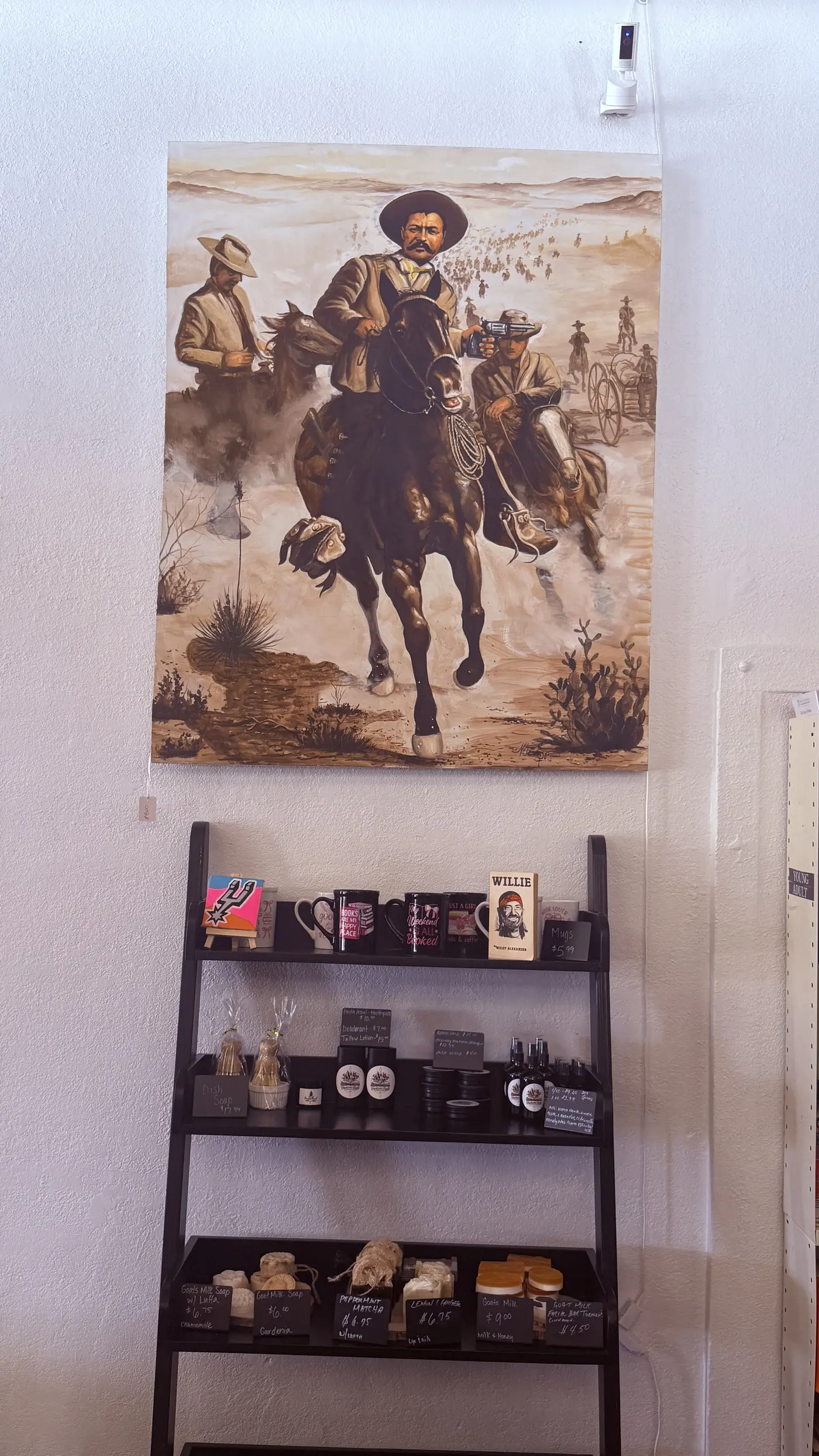 Western-themed painting of riders on horseback hanging above a shelf of goat's milk soaps and homegrown goods.