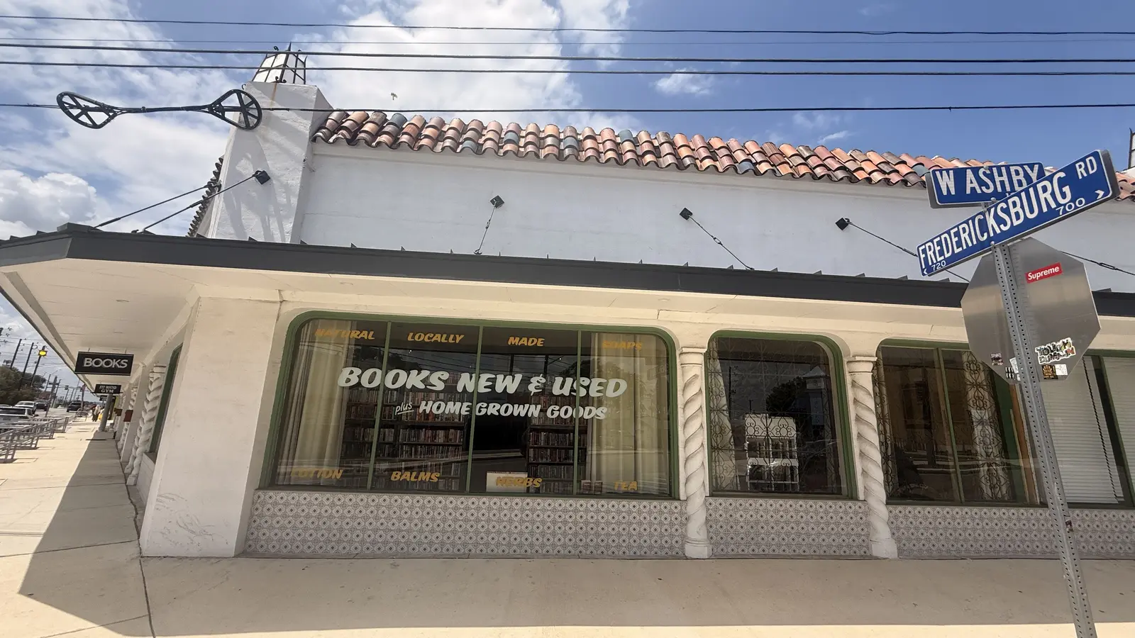 Wide corner view of the storefront with the W Ashby and Fredericksburg Road street signs.