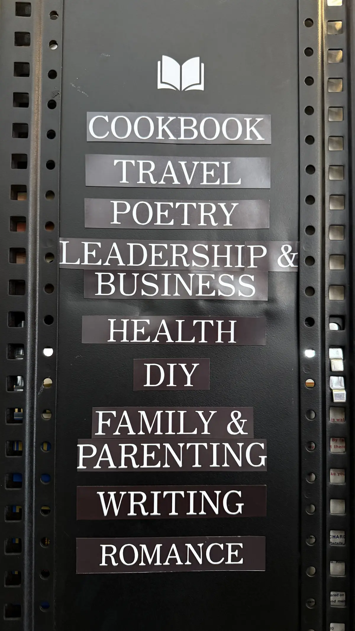 Hand-labeled genre signs reading Cookbook, Travel, Poetry, Leadership & Business, Health, DIY, Family & Parenting, Writing, and Romance.