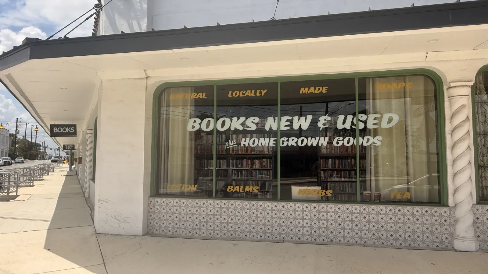 Angled sidewalk view of the storefront with the hanging BOOKS sign and green window trim.