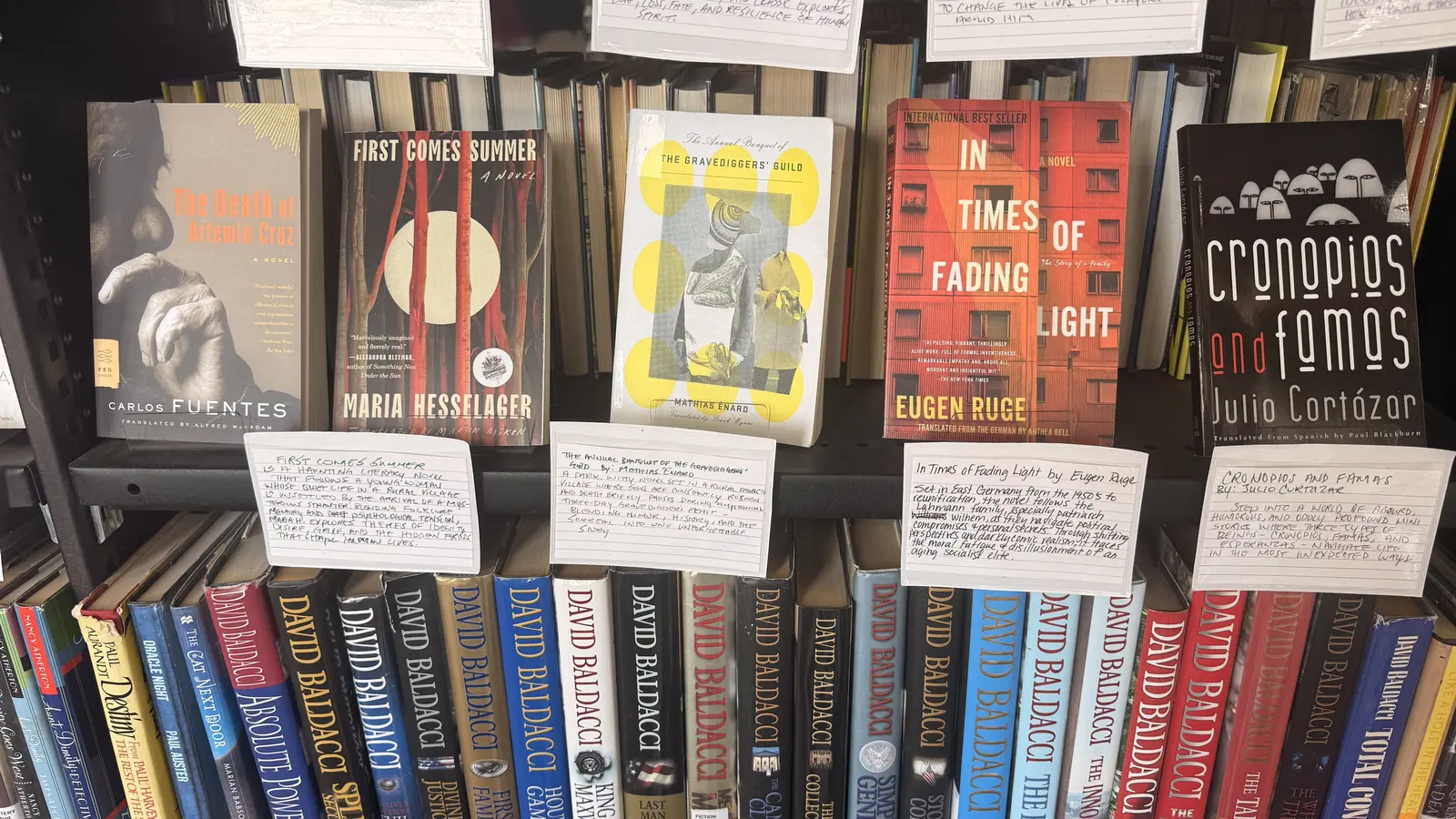 Staff picks shelf with handwritten recommendation cards for The Death of Artemio Cruz, First Comes Summer, The Annual Banquet of the Gravediggers' Guild, In Times of Fading Light, and Cronopios and Famas.