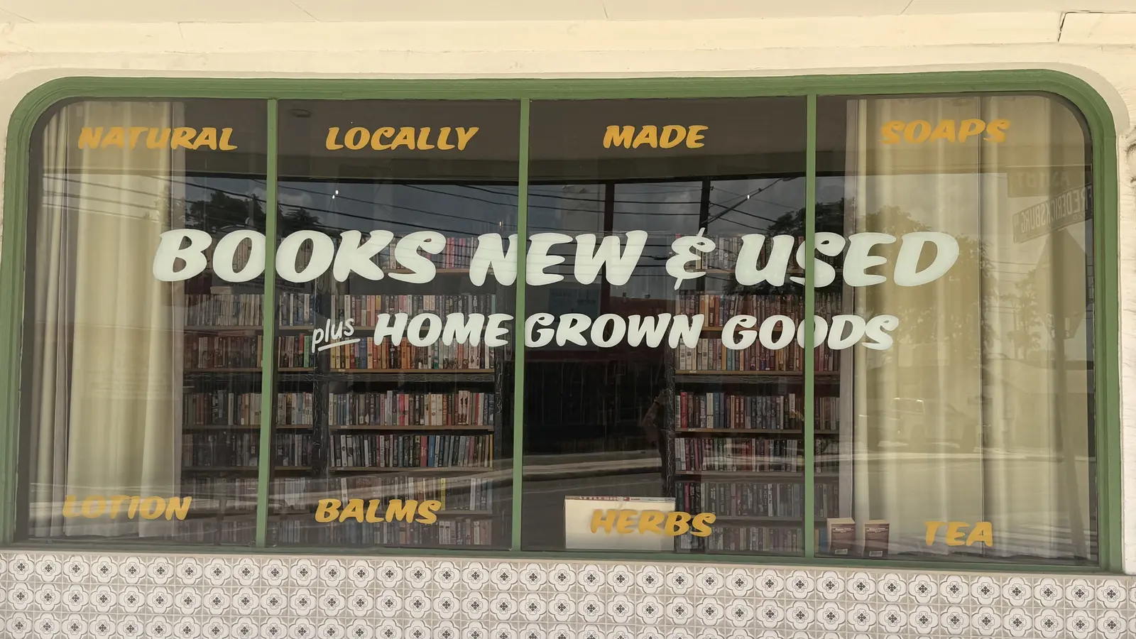 Close-up of the Books New & Used, plus Home Grown Goods window lettering with bookshelves visible inside.